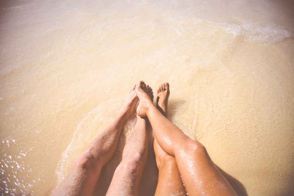woman and man's legs in the sea whilst sitting on beach