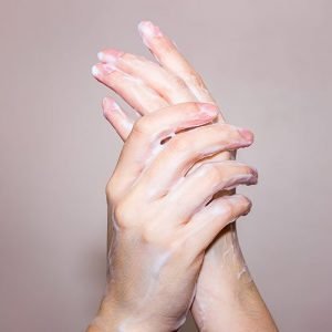 Square image of hands covered in cream on grey background