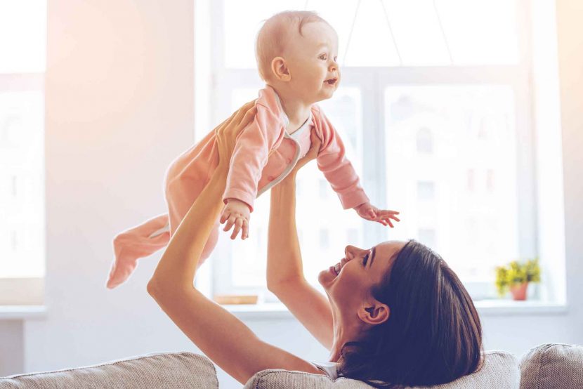 woman smiling which holding baby in the air