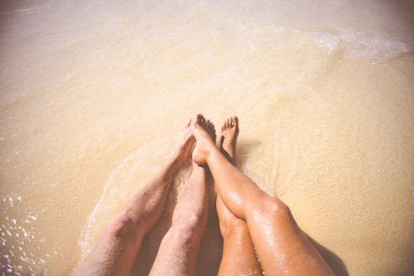 woman and man's legs in the sea whilst sitting on beach